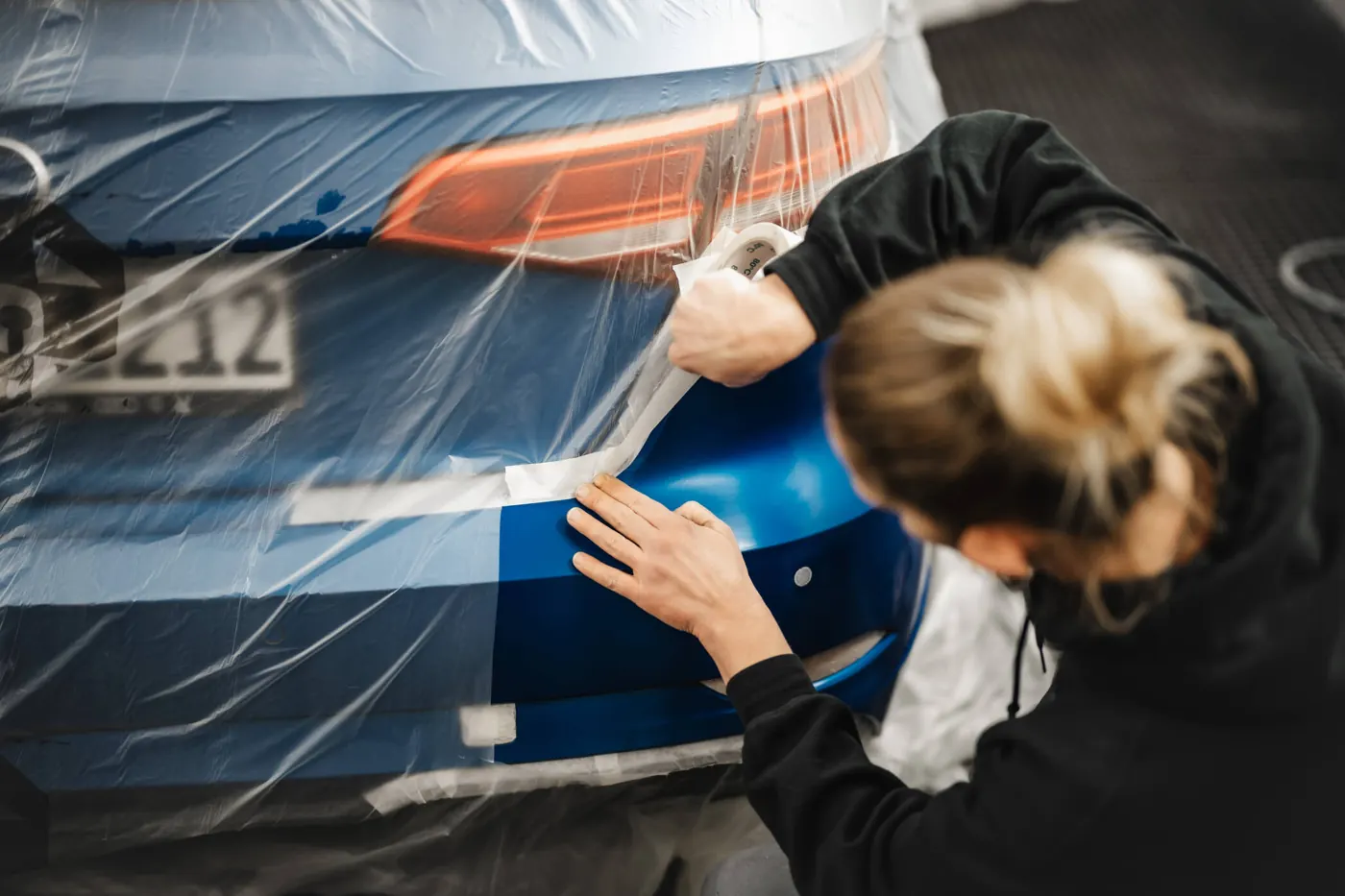 Lackiererin klebt die Stoßstange eines blauen Fahrzeugs ab